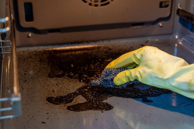 Hand in a rubber glove cleaning dirty oven with sponge and cleaner. Housework and housekeeping concept