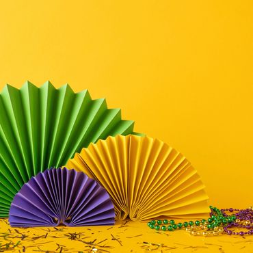 Colorful paper fans and Mardi Gras beads against a vibrant yellow background.