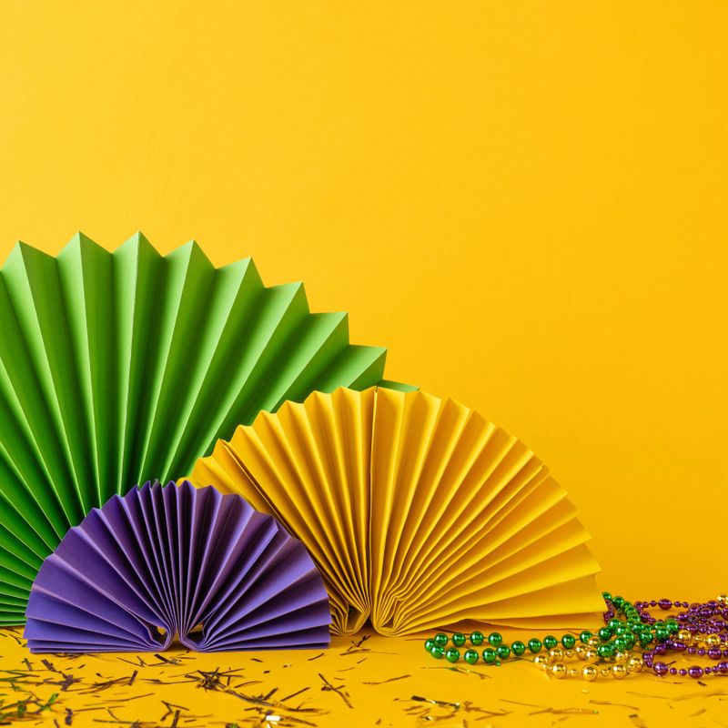 Decorative side vertical view paper fans in green, yellow, and purple alongside beads celebrating Mardi Gras
