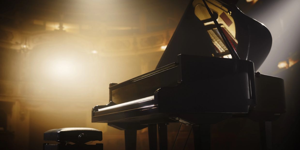 A grand piano illuminated by soft stage lighting in a concert hall.