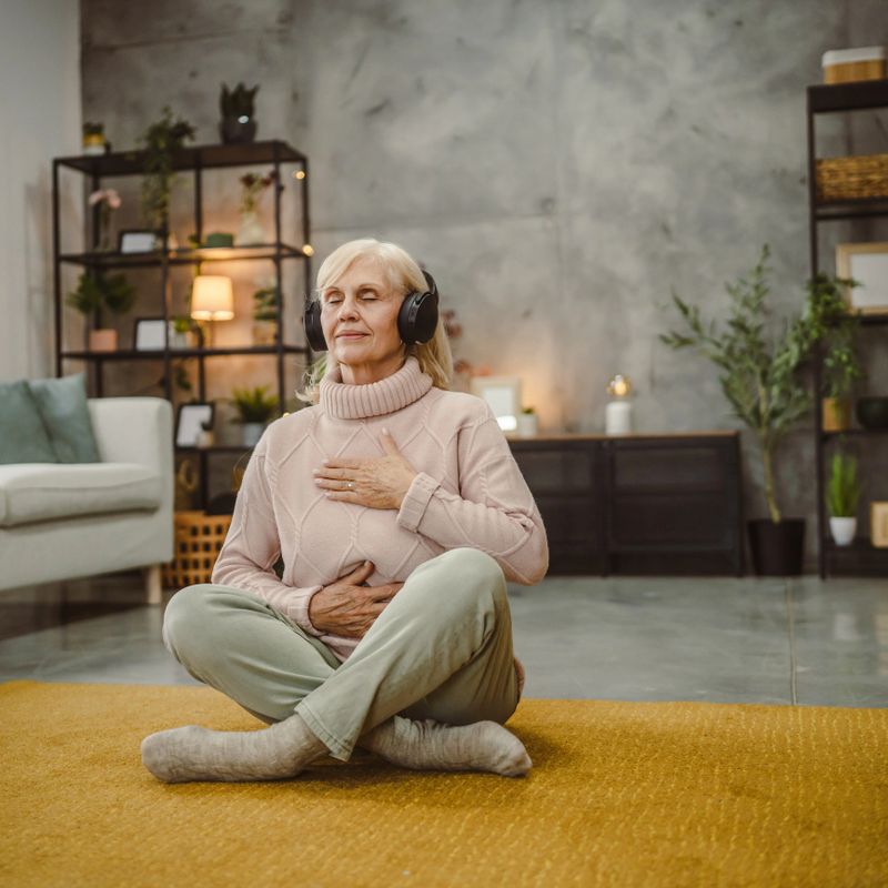 senior woman eyes closed have guided training yoga or meditation while sit on floor with headphones