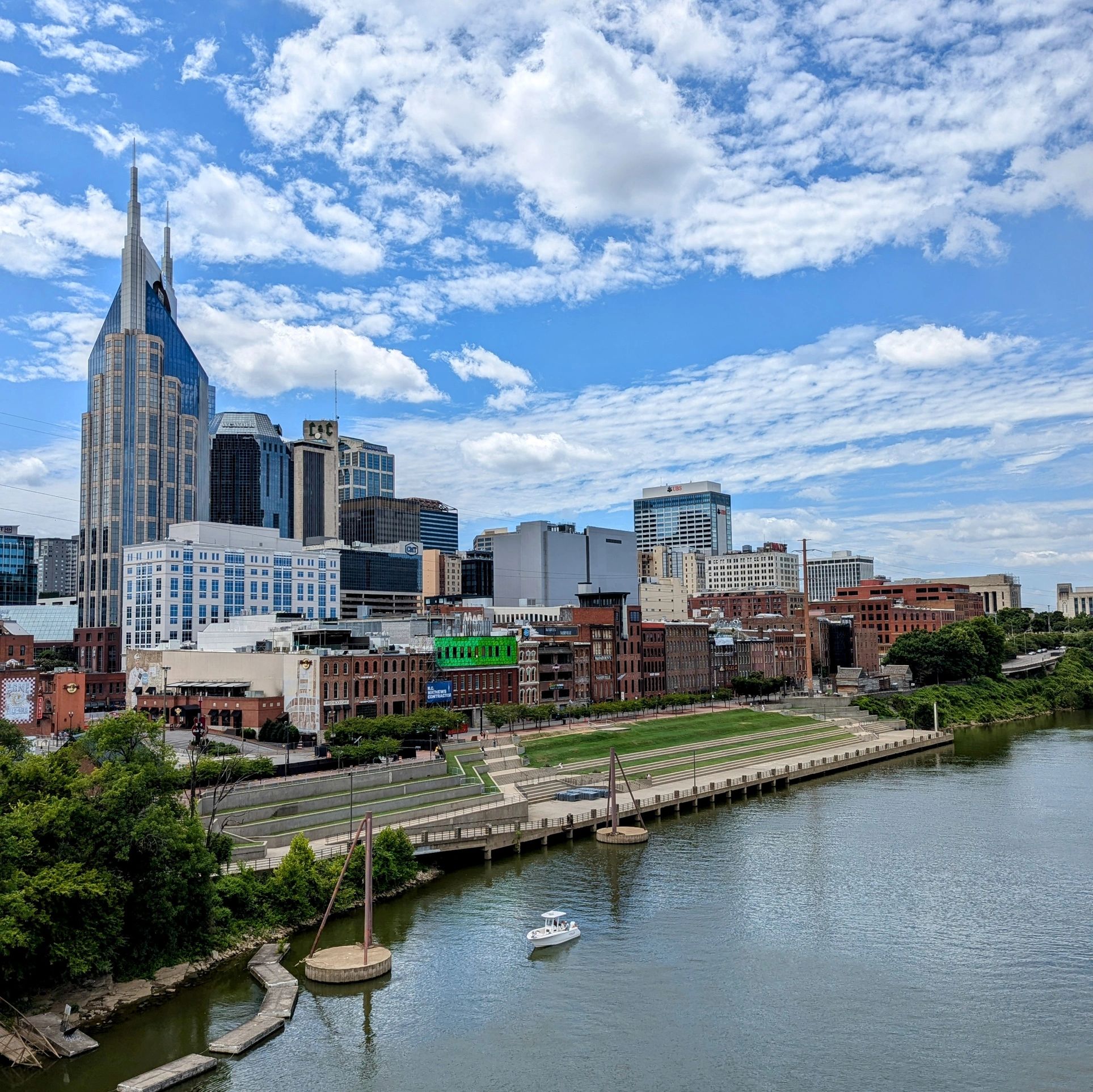 City skyline with a river and a boat under a partly cloudy sky.