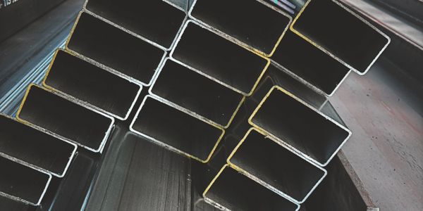 Stacked rectangular metal pipes in an industrial setting.
