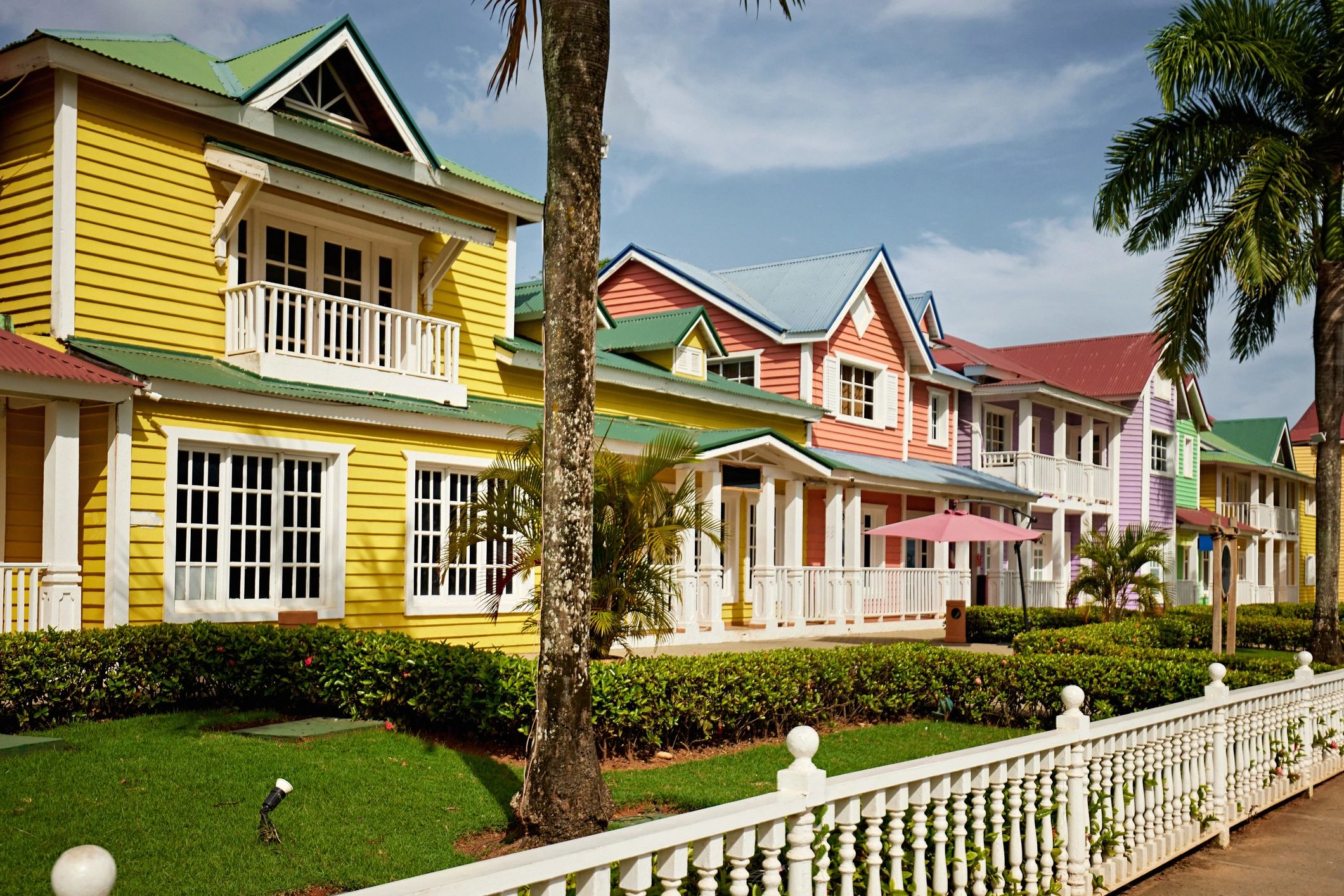 Colorful pastel houses with white trim and green lawns under a blue sky.