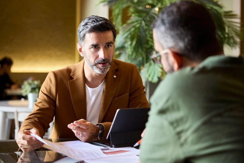Manager explaining documents to colleague in meeting. Entrepreneurs are planning business strategies. They are at coworking space.