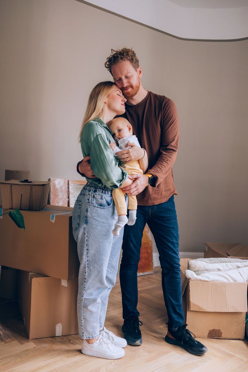 Loving family embracing together while holding their baby, surrounded by unpacked boxes in their cozy home. Depicts warmth, parenthood, and the start of a new chapter in life.