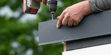 Person using a power drill to fasten a board outdoors.