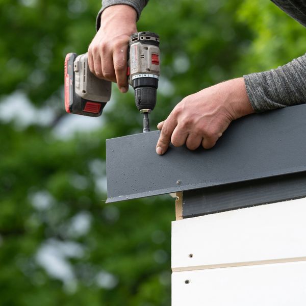 Person using a drill to fix a metal sheet on the edge of a structure.