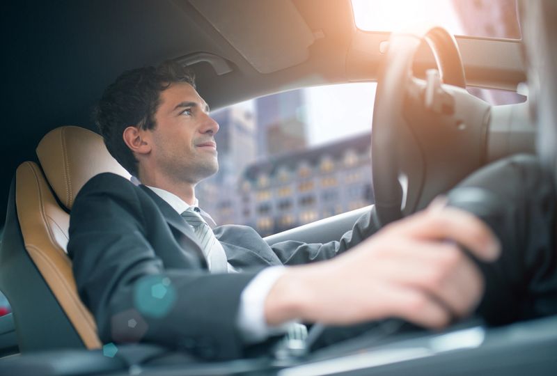Young businessman driving a sleek electric car through the bustling city center, glancing out the window with a confident expression, embodying success and ambition