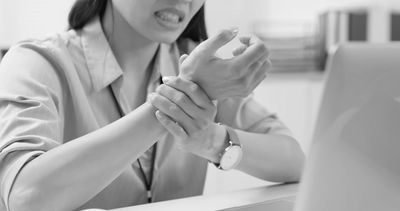 Woman clutching her wrist in pain at a desk.