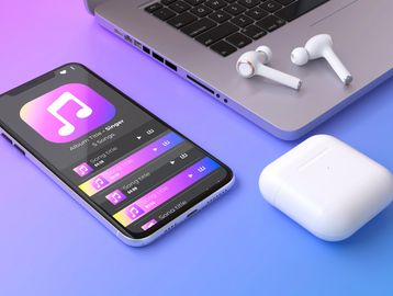Smartphone playing music with wireless earbuds and laptop nearby.