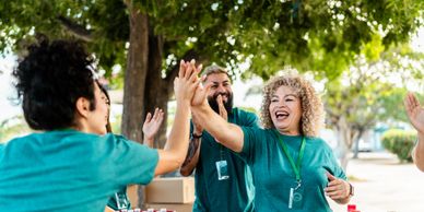 Volunteers joyfully high-five outdoors during a community event.