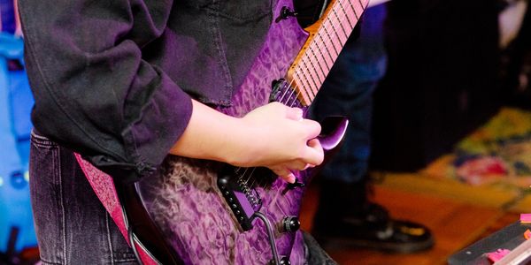 Person playing a purple electric guitar with focus on hands and instrument.