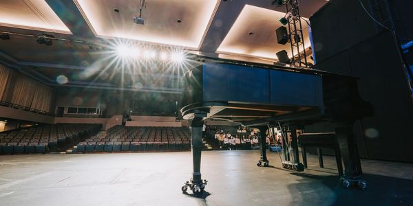 A grand piano on an empty stage with bright lights.
