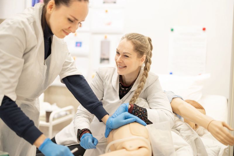 Two healthcare professionals nurses collaborate while practicing medical techniques on a mannequin in a clinical environment
