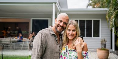 Happy couple smiling outside a modern house with friends in the background.
