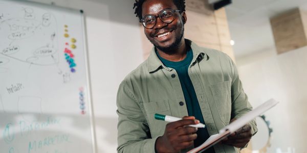 Smiling man holding a marker and clipboard in a bright office.