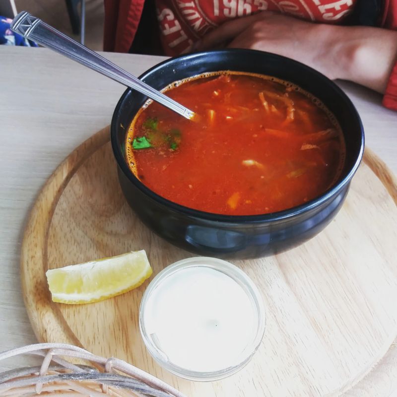 Enjoy a vibrant bowl filled with spicy soup, accompanied by fresh lemon and savory sauce, ideal for a flavorful meal