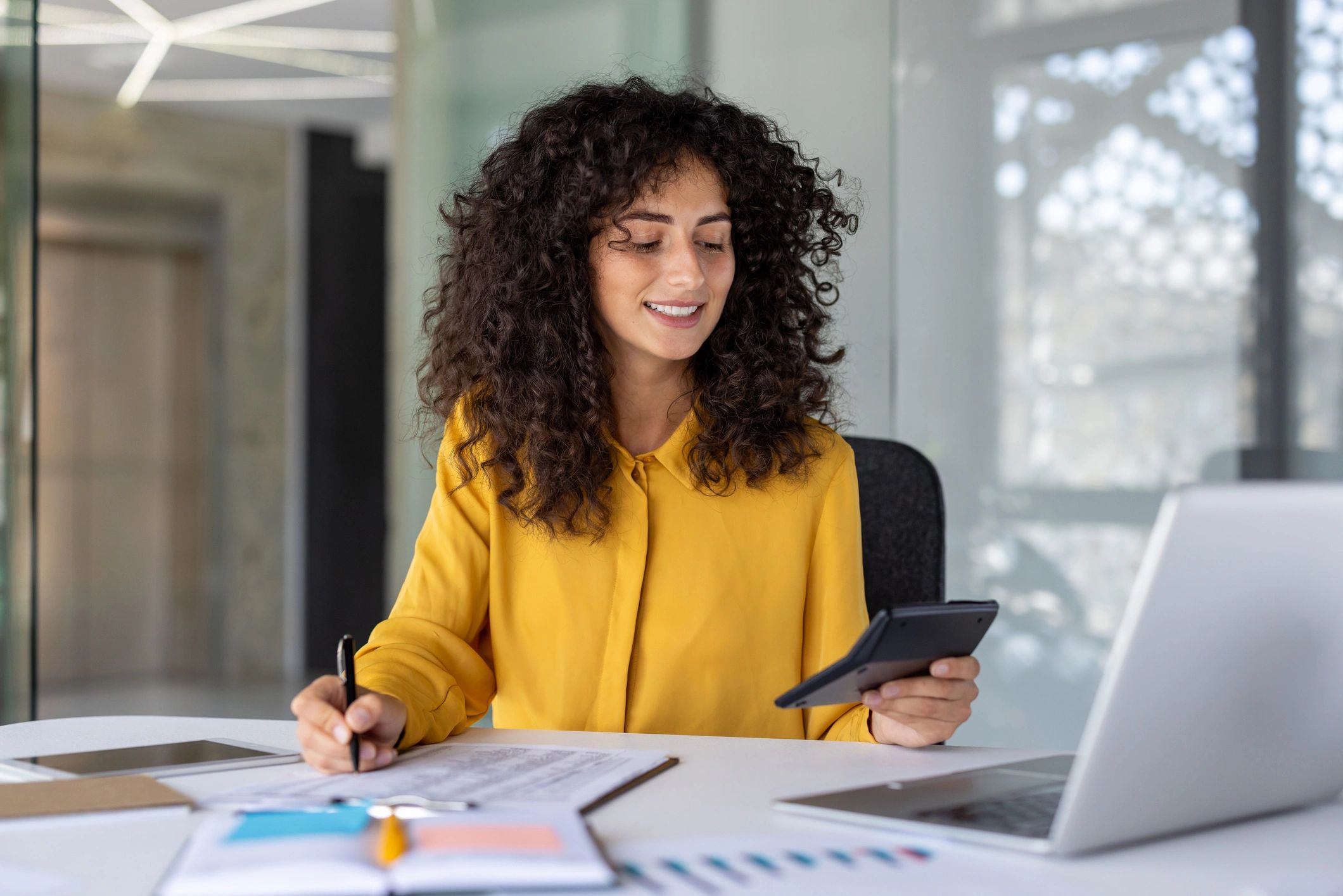 Woman in yellow shirt working with a calculator and documents.