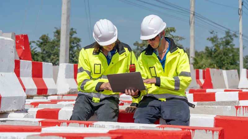 A Caucasian white civil engineer, architect, or construction worker is wearing a safety suit while inspecting building construction on site and verifying blueprints or drawing plans.