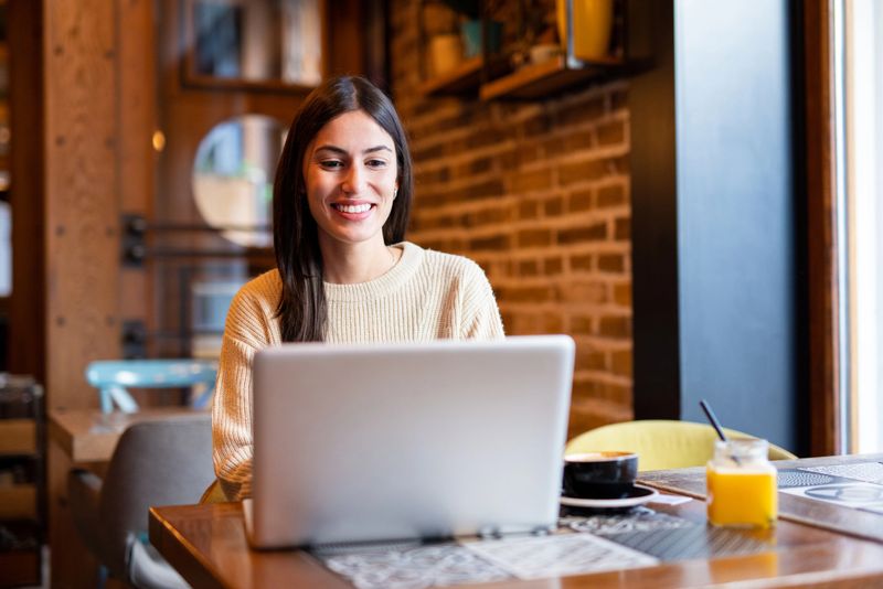 Beautiful smiling woman using laptop, sitting in interent cafe.