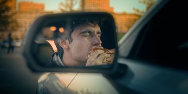 Man enjoying a burger, reflected in a car's side mirror.