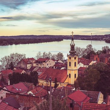 A peaceful town with a church tower near a river at sunset.