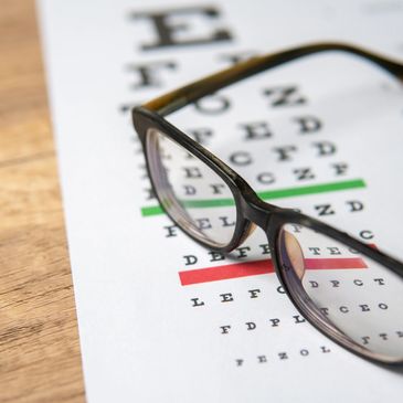 Glasses resting on an eye chart with green and red lines on a wooden table.
