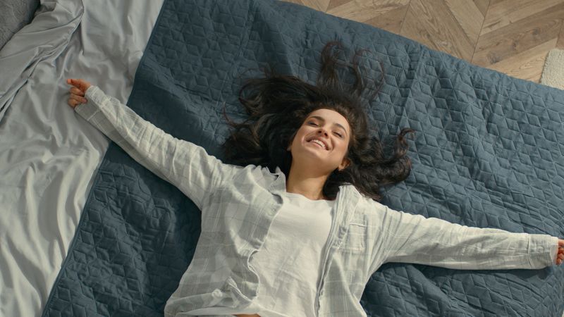 Top view Caucasian Young woman brunette fall on bed rest pleasure happiness smile laughter fun girl bedroom domestic lifestyle carefree lady enjoy positive relaxed lying soft mattress cozy comfortable. High quality 4k footage