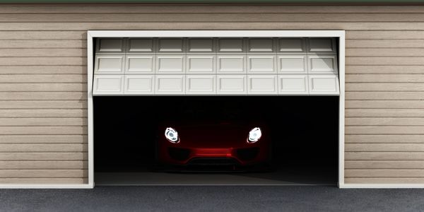 Sports car with headlights on, inside a partially open garage.