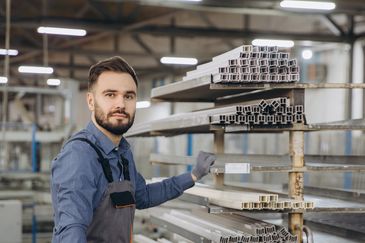 Worker inspecting metal profiles in a factory.