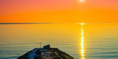 Sunset over calm waters with a rocky pier in the foreground.