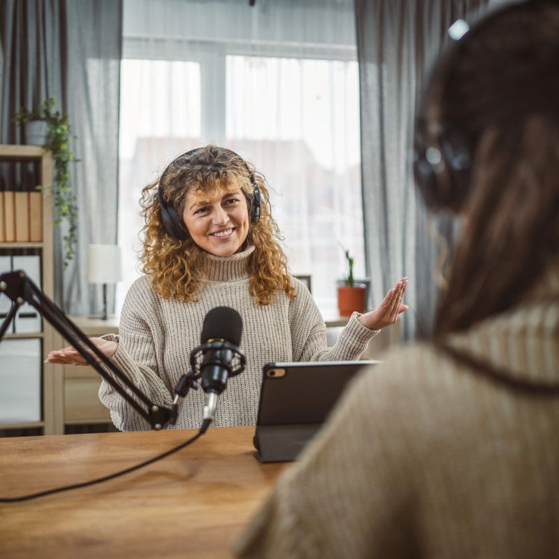 adult woman presenter interview female guest and stream audio podcast use microphone and laptop at home broadcast studio