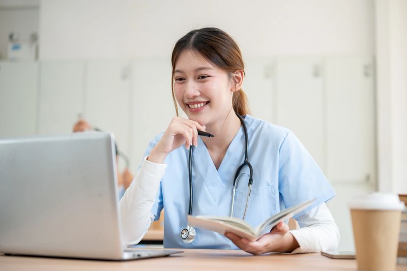 A pretty and smart Asian female medical student in scrubs is focused on reading medical cases on her laptop while attending a lecture with a professor in the classroom.