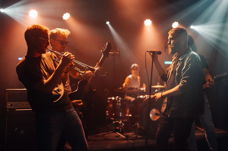 Vibrant stage with colorful spotlights, band performing live with guitars, drums, trumpets, and microphones, playing rock, pop, jazz, blues, and other genres