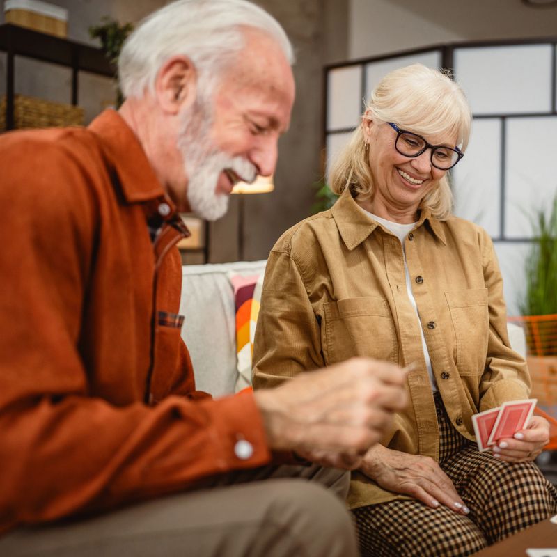senior couple husband and wife play cards at home in bright day leisure games concept