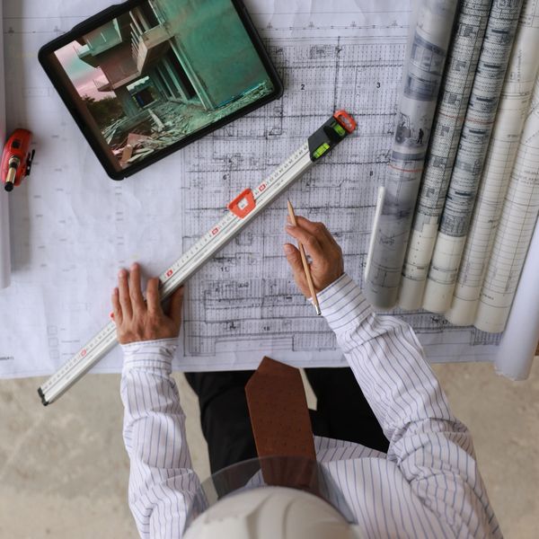 Architect reviewing building plans with digital tablet and measuring tools on a desk.