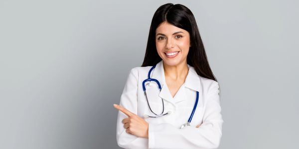 Smiling female doctor pointing to the side, wearing a white coat and stethoscope.