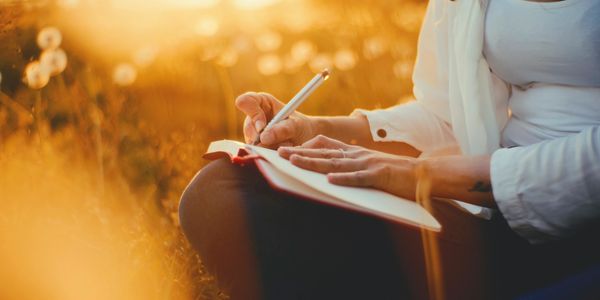 Person writing in a notebook outdoors during golden hour.
