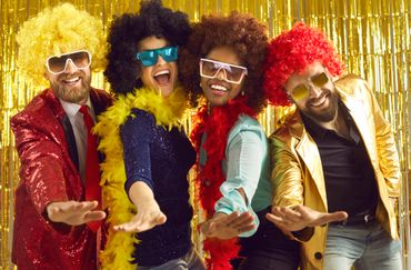 Four friends in colorful wigs and flashy outfits having fun at a party.