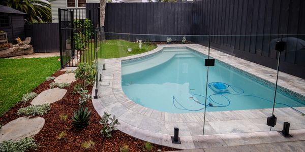 A modern backyard pool with clear glass fencing and landscaped garden.