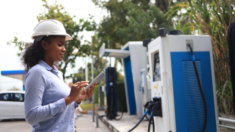 A Black female Electrical engineer is examining the electric vehicle charging pile, EV charger , green Zero carbon energy