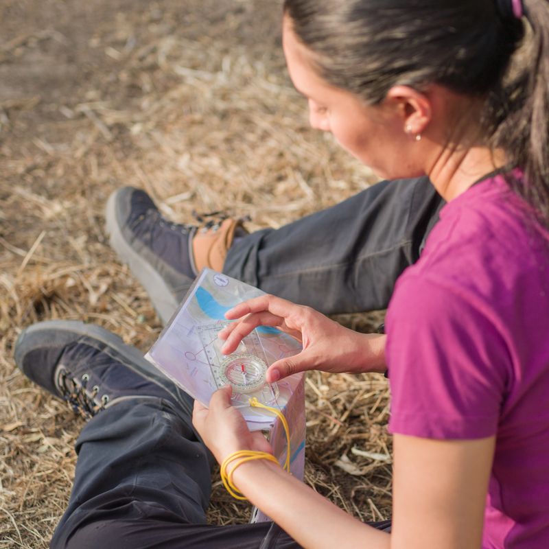 Young woman navigating the countryside with a map and compass during an orienteering race, embracing adventure and the outdoors