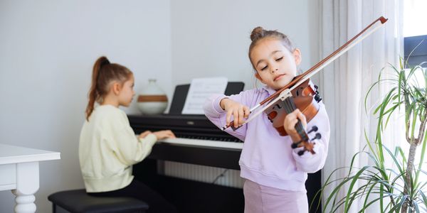 Two girls practicing music, one playing violin and the other piano.