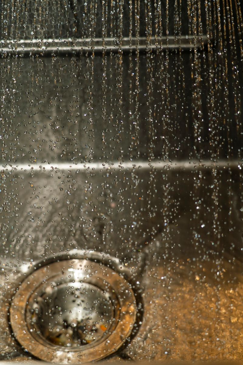 Water flows from a showerhead, creating a beautiful cascade of droplets that fall into a drain, highlighting the simplicity of a bathroom setting.