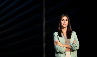Confident woman standing with arms crossed in a dark setting.