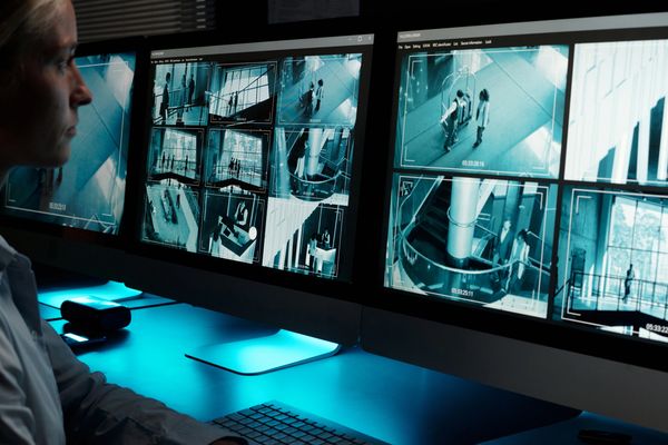 Person monitoring multiple security camera feeds on computer screens.