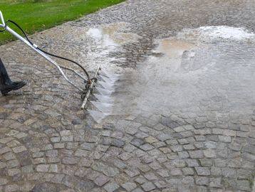 Cleaning cobblestone pavement with a pressure washer.