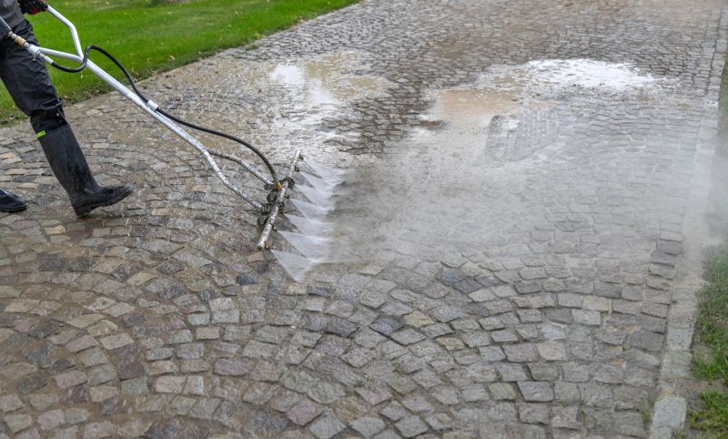 Cleaning service worker washing cobblestone pavement with pressure washer