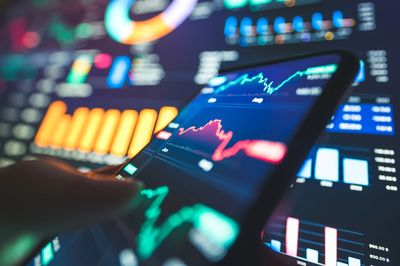 Smartphone showing financial graphs with colorful charts in background.